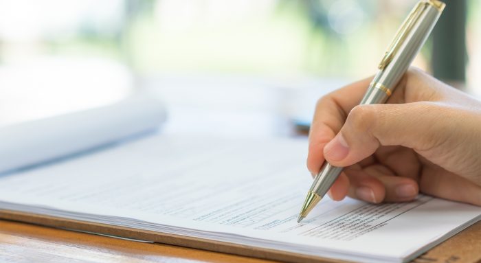 Hand with pen over application form . Hand with pen over application form